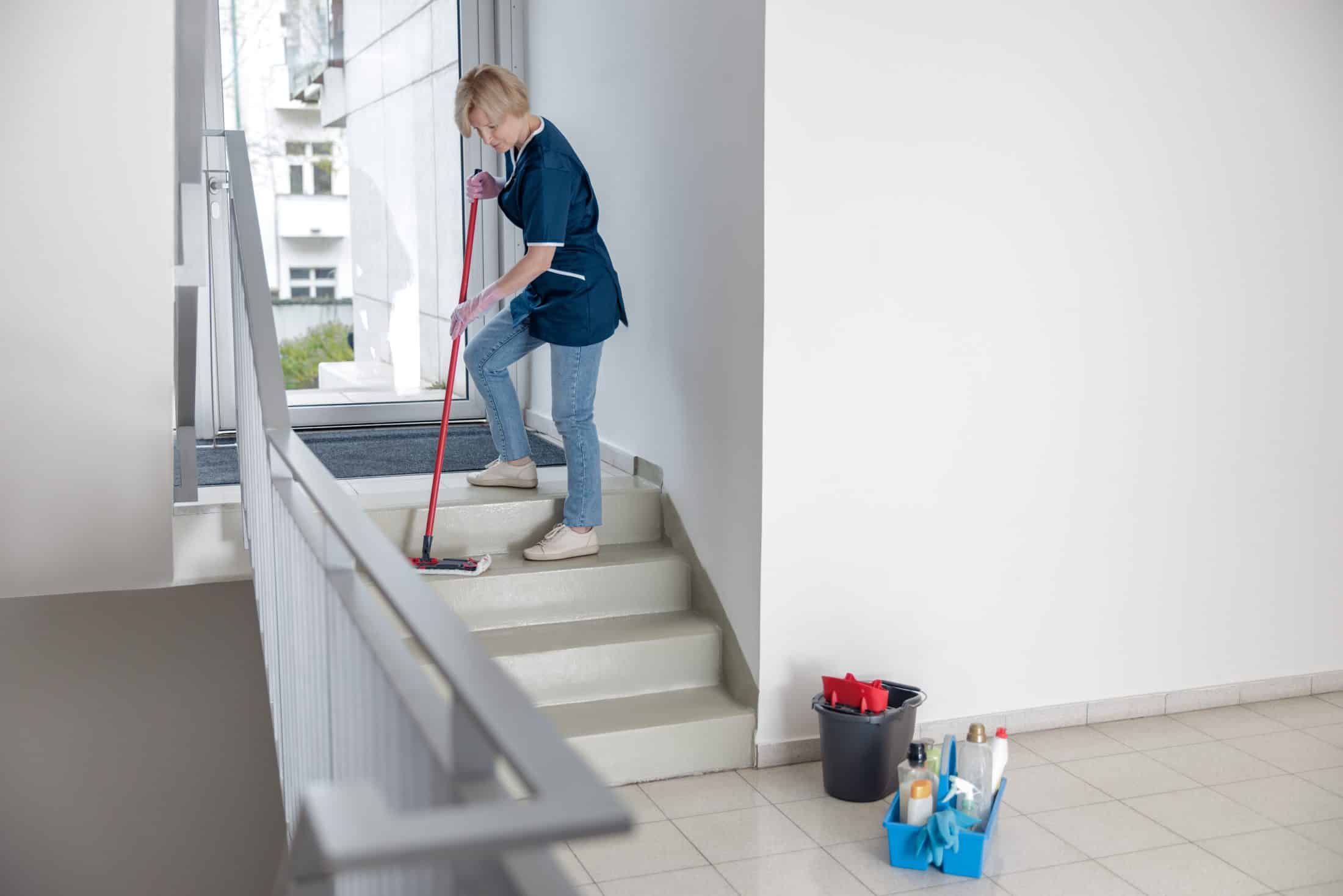 Putzfrau in Uniform mit Mopp und Lappen wäscht eine staubige Treppe des Hauses. Foto in hoher Qualität